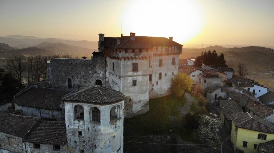 Il castello di Mornese (AL) visto dall'alto con il sole basso all'orizzonte. I tetti delle case sul lato destro del castello quasi si confondono con la vegetazione brulla autunnale