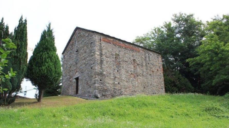 Briga Novarese (NO). Dal prato verdeggiante, fra alberi ricchi di fogliame si erge la piccola e antica chiesetta di San Tommaso in stile romanico. Fotografia di Carlo Moroso.