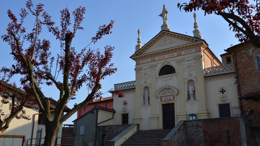 Scurzolengo (AT). Una scalinata accompagna al portale di ingresso della Chiesa parrocchiale barocca di San Lorenzo. La Chiesa è incorniciata da due alberi in fiore. Il cielo è limpido.