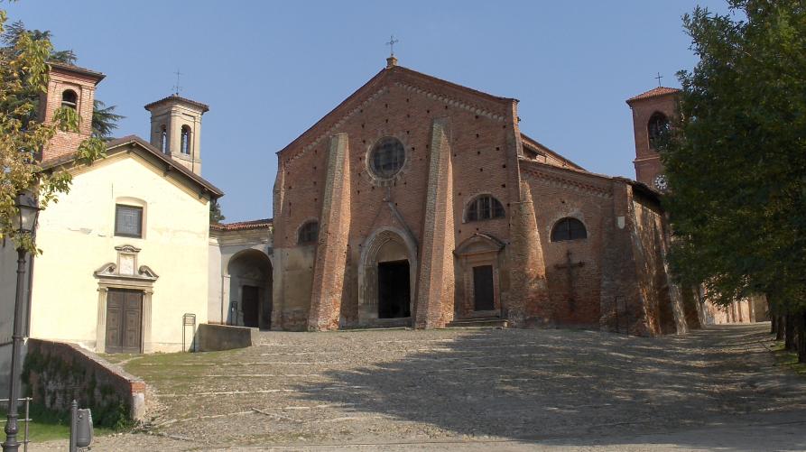 Cassine (AL). Il piazzale leggermente in salita conduce alla facciata gotica, in mattoni rossi, della Chiesa di San Francesco. A destra alcuni edifici più bassi e a destra una fila di alberi. Fotografia di Sergio Arditi (2013) 