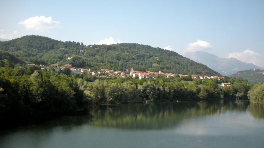 Vidracco (TO). Il paese in lontananza visto dal lago e immerso nella vegetazione rigogliosa. Il cielo azzurro è macchiato da qualche ciuffo di nuvole bianche 