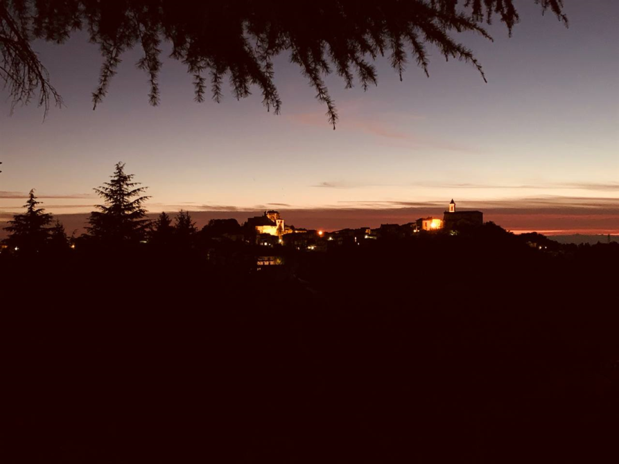 Mornese (AL). Panorama notturno. Immagine tratta dal sito del Comune. Il paese di Mornese che si intravede in lontananza è immerso nel buio serale. Le poche luminarie del paese e gli ultimi raggi di luce mettono in risalto le forme degli edifici in contrasto con il cielo grigio rosato. 