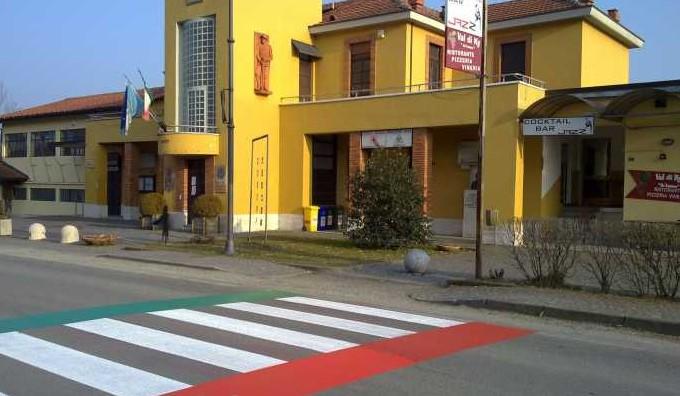  Vidracco (TO). Le strisce pedonali bianche con banda laterale verde a sinistra e banda laterale rossa a destra, conducono al municipio color giallo zafferano. Fotografia tratta dal sito del Comune (2025) 