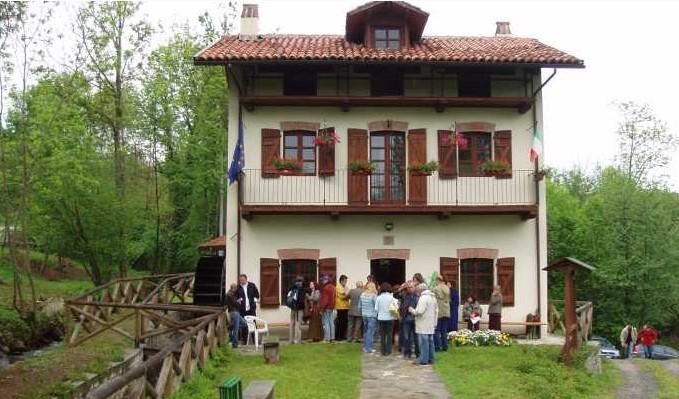 Vidracco (TO). Ecomuseo dell'acqua e degli antichi mestieri. Un vecchio mulino a due piani completamente restaurato. La facciata è color crema, i serramenti sono in legno e il tetto in tegole rosse. Gli alberi affiancano la casa destra e a sinistra. Fotografia tratta dal sito del Comune (2025) 