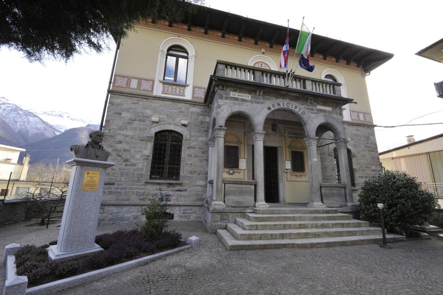 Premosello-Chiovenda (VCO). La facciata del Municipio. Il primo piano è rivestito di pietra grigia, come la scalinata che porta all'atrio abbellito da tre arcate. Il secondo piano, dipinto colo crema, ha tre finestre ad arco.  