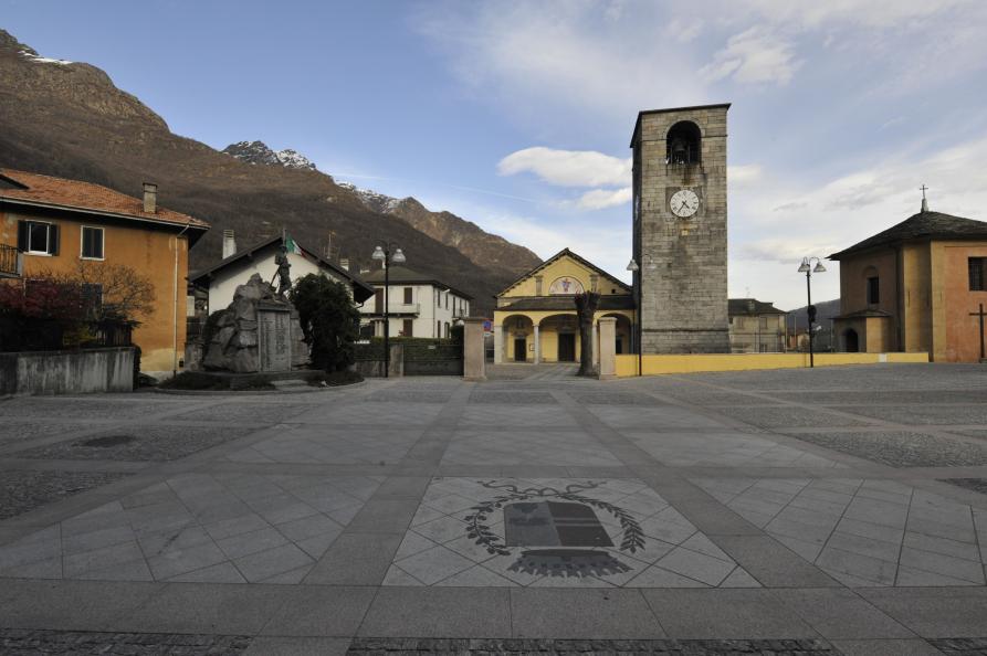 Premosello-Chiovenda (VCO). Ampio piazzale in primo piano. Al fondo la torre romanica e la Chiesa Parrocchiale dell’Assunta 
