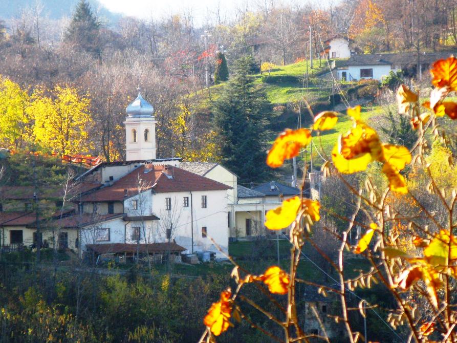 Boves (CN). Collina di Sant'Antonio. Il campanile bianco svetta dai tetti in mattoni rossi delle case tinteggiate di bianco. Il bosco autunnale fa da cornice. Fotografia di Giorgio Vannucchi 