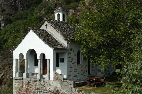 Premosello-Chiovenda (VCO). La piccola Cappella del Lut. I muri bianchi della facciata sono abbelliti da tre arcate e spiccano fra la ricca vegetazione 