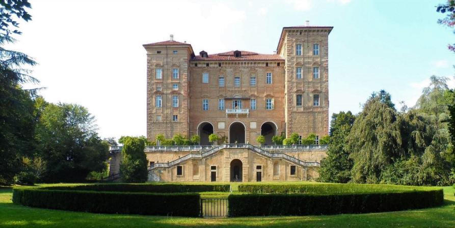 Agliè (TO). Il giardino introduce la doppia scalinata che porta all'entrata con i tre archi del Castello ducale. Due torri laterali incorniciano la parte centrale del palazzo in mattoni a vista.Fotografia tratta dal sito del Comune (2025). 