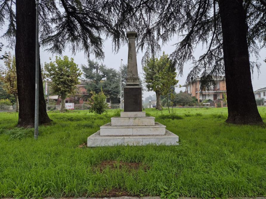 Villalvernia (AL). Sul manto erboso quattro gradini in marmo bianco sostengono una colonna alla cui base, su lastra di bronzo, sono elencati i nomi dei caduti della Prima guerra mondiale. Fotografia tratta dal sito del Comune (2025) 