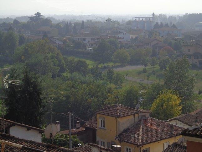 Villalvernia (AL). In basso alla foto un caseggiato giallo con tetti rossi. Più in alto alberi e giardini con siepi e in lontananza costruzioni rurali e più moderne immerse nel verde. Fotografia di Elisabetta Spotorno 