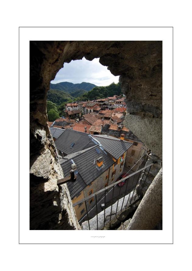 Arola (VCO). Scorcio del centro storico con vista dall'alto dei tetti del centro abitato. In lontananza le montagne verdi. Fotografia di Enzo Franza (2013) 