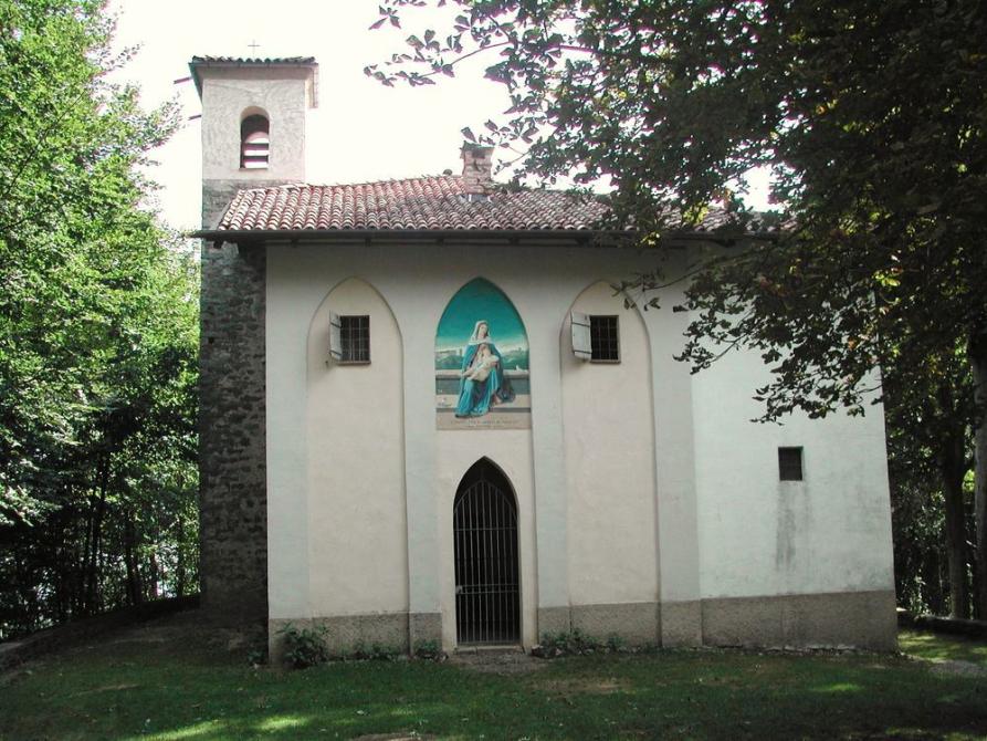 Camandona (BI). Tra la vegetazione spicca il piccolo santuario del Mazzucco dedicato a S. Anna. A sinistra il campanile sottile in pietre grigie. Al Santuario si accede tramite una porta con arco acuto: sulla sua sommità l'immagine dipinta della Santa. Fotografia di Ilario Guelpa Piazza 