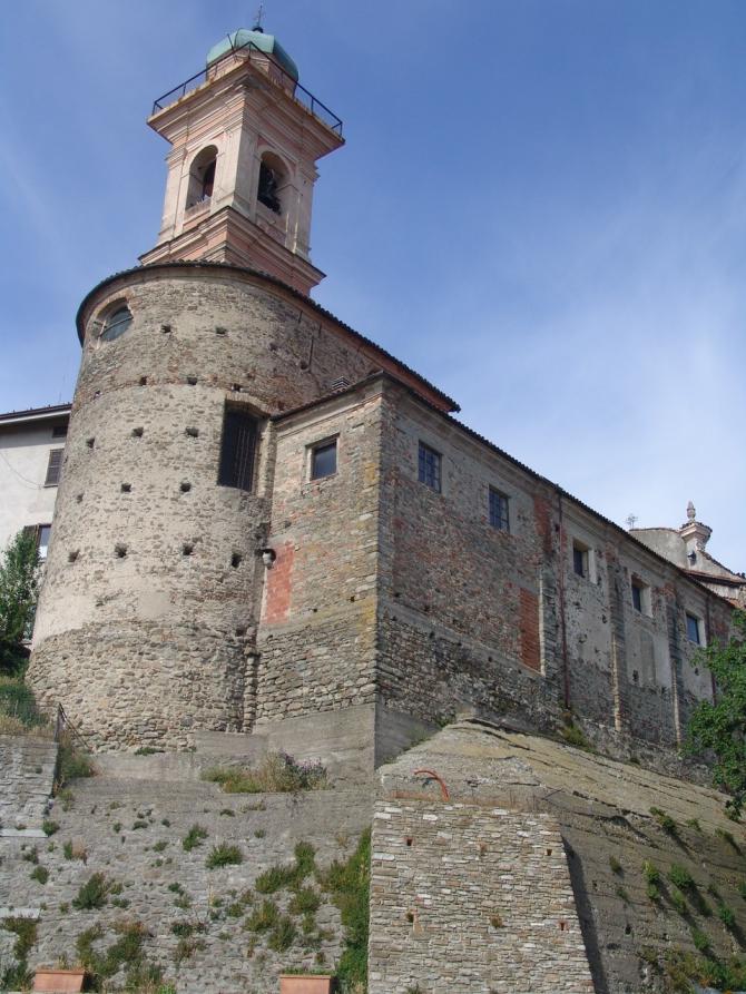 Pareto (AL). Inquadratura del retro delle mura in pietra della Chiesa di San Pietro da cui svetta la porzione terminale del campanile barocco con guglia rivestita in rame. Immagine tratta dal sito del Comune 