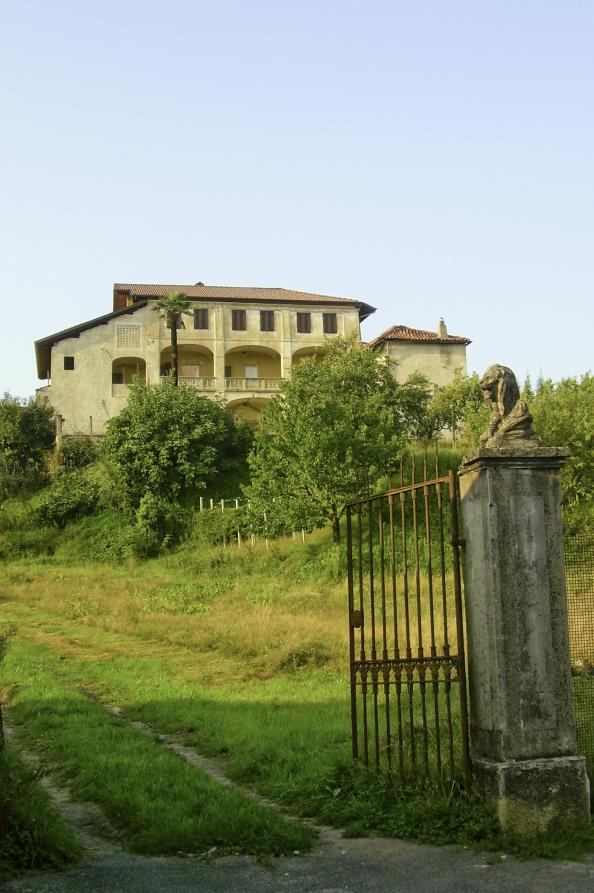 Lozzolo (VC). Da un vecchio cancello in ferro battuto con leone in cemento seduto sulla colonna di destra si inerpica un sentiero che conduce alla casa parrocchiale che domina la collina 