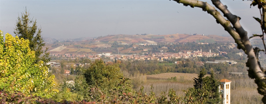 Farigliano (CN). Vista del paese in lontananza e delle sue colline coltivate. Il cielo non è limpido e c'è una leggera foschia.  