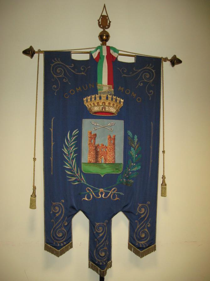 Momo (NO). Bandiera quadrata (un drappello) che porta le armi del comune così descritte: "Di azzurro al castello di rosso, torricellato in un pezzo centrale, merlato alla guelfa aperto e finestrato, fondato sulla campagna di verde, cimato da due mazze ferrate di argento poste in croce di S.Andrea". Fotografia di Laura Colombo (2009) 