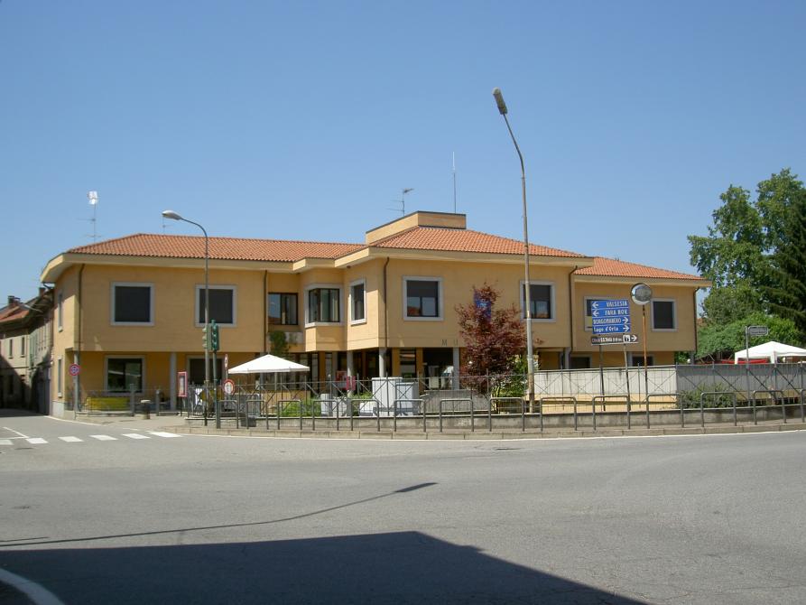 Momo (NO). Vista dalla strada della struttura moderna del Municipio a due piani tinteggiato colo crema. Il cielo è limpido e luminoso. Fotografia di Luciano Amaranto (2007) 