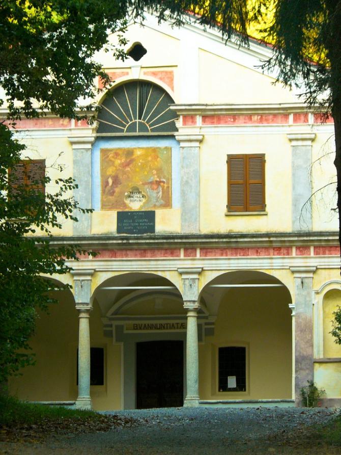 Lozzolo (VC). Incorniciata dalle fronde degli alberi spicca la facciata dipinta e decorata del Santuario della Madonna Annunziata. Tre arcate conducono all'entrata. In alto due finestre con scuri dei legno chiusi e un mezzo rosone con spicchi di vetro 