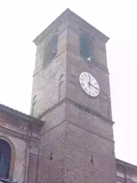 Gamalero (AL). Inquadratura dal basso della torre campanaria della Chiesa di San Lorenzo.  Il campanile è in mattoni rossi e presenta orologio e monofora terminale da cui si intravedono le campane 