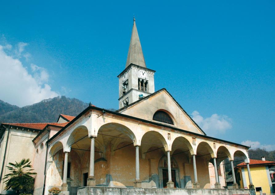 Nonio (VCO). In primo piano la Chiesa parrocchiale di San Biagio con un ampio portico con colonnato. Si intravede la porzione finale del campanile che termina con cuspide piramidale. Sullo sfondo il cielo blu e le cime delle montagne. Fotografia di Daniele Ciocca 