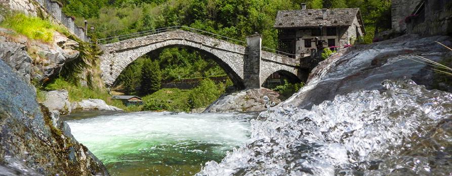 Rassa (VC). Sotto l'antico ponte in pietra grigia scorre il torrente. A destra una piccola casa dalle caratteristiche mura in pietra. Immagine tratta dal sito del Comune (2023) 
