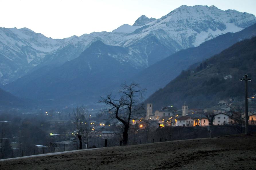 Villar Pellice (TO). Dopo il tramonto il crepuscolo tinge le montagne di azzurro. Il paese in lontananza è leggermente illuminato dai lampioni. Svetta centrale un albero spoglio in siluette 