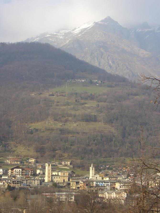 Villar Pellice (TO). Panoramica verticale sul paese visto in lontananza. Le montagne sullo sfondo sono brulle. Il cielo è grigio 