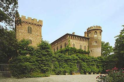 Masio (AL). Il castello di Redabue è immerso nella natura verdeggiante. A sinistra una torre quadrata, al centro il corpo centrale del castello e a destra una torre a pianta circolare. Il cielo è azzurro 