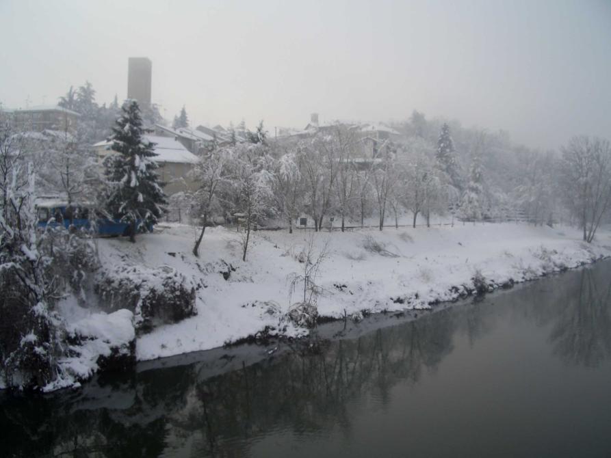 Masio (AL). Immagine invernale del Tanaro che scorre sulla destra. La riva sinistra è innevata e il paese, in lontananza, è coperto di candida neve  