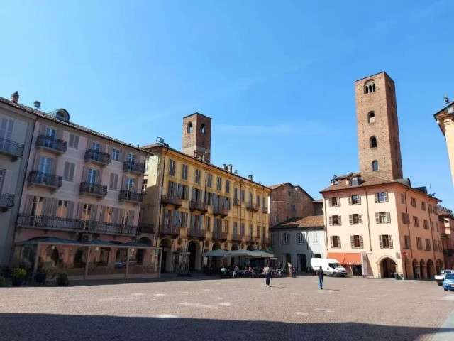 Alba (CN). Piazza Risorgimento con gli edifici storici e le due torri che spiccano dai tetti. Il cielo è azzurro. Fotografia tratta dal sito del Comune (2024) 