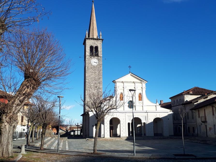 Vigliano Biellese (BI). La Chiesa di Santa Maria Assunta e il suo campanile romanico in pietra grigia con cuspide piramidale. Il cielo è blu intenso 