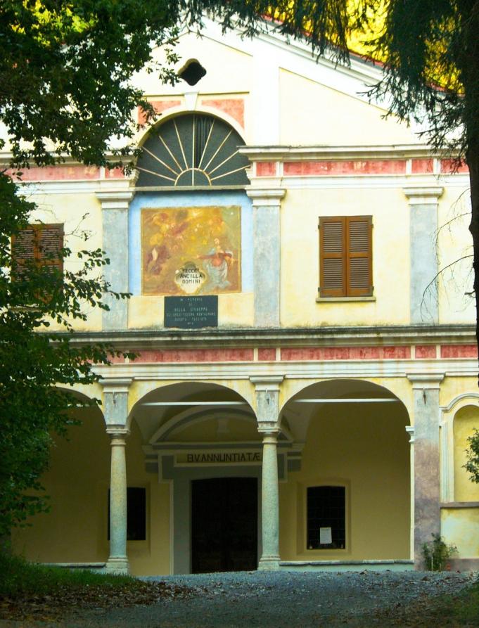 Lozzolo (VC). Incorniciata dalle fronde degli alberi spicca la facciata dipinta e decorata del Santuario della Madonna Annunziata. Tre arcate conducono all'entrata. In alto due finestre con scuri dei legno chiusi e un mezzo rosone con spicchi di vetro 