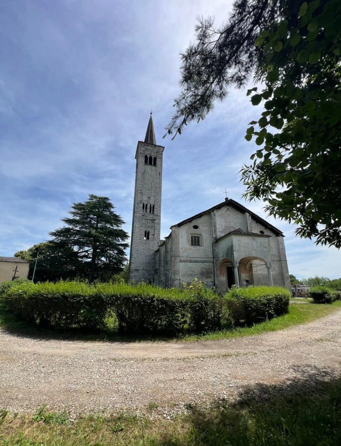 Ameno (NO). Dalla strada sterrata si vede la chiesa parrocchiale di Maria Vergine Assunta e il campanile in pietra a vista. Fotografia di Mauriliano Castiglioni (2026)  