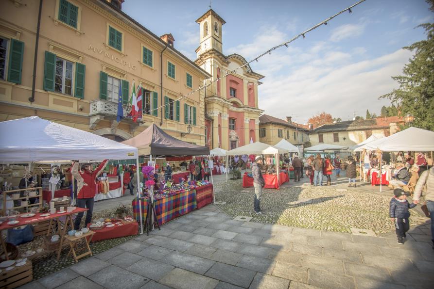 Ameno (NO). A sinistra la facciata del municipio affiancato dall'Oratorio di San Giovanni Battista. Piazza Marconi ospita alcuni banchi in occasione di una fiera 
