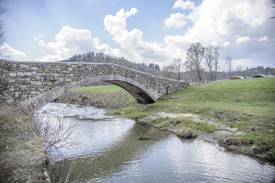 Ameno (NO). Il torrente Agogna scorre placido sotto il ponte romanico. In lontananza si intravede la cima di una collina. Il cielo è solcato da nuvoloni bianchi 