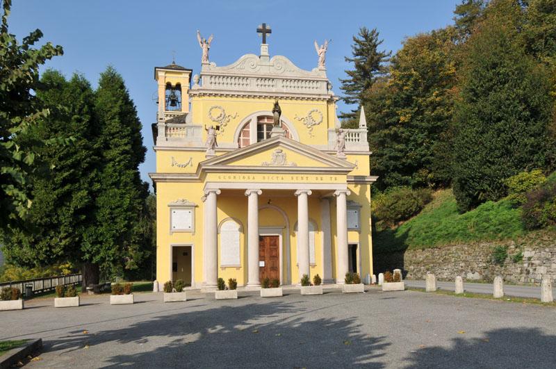 Ameno (NO). Fra la vegetazione svetta il santuario Madonna della Bocciola in stile neoclassico. Le pareti dipinte color crema e decorate con fregi e coccarde. All'entrata un portico con quattro colonne. 
