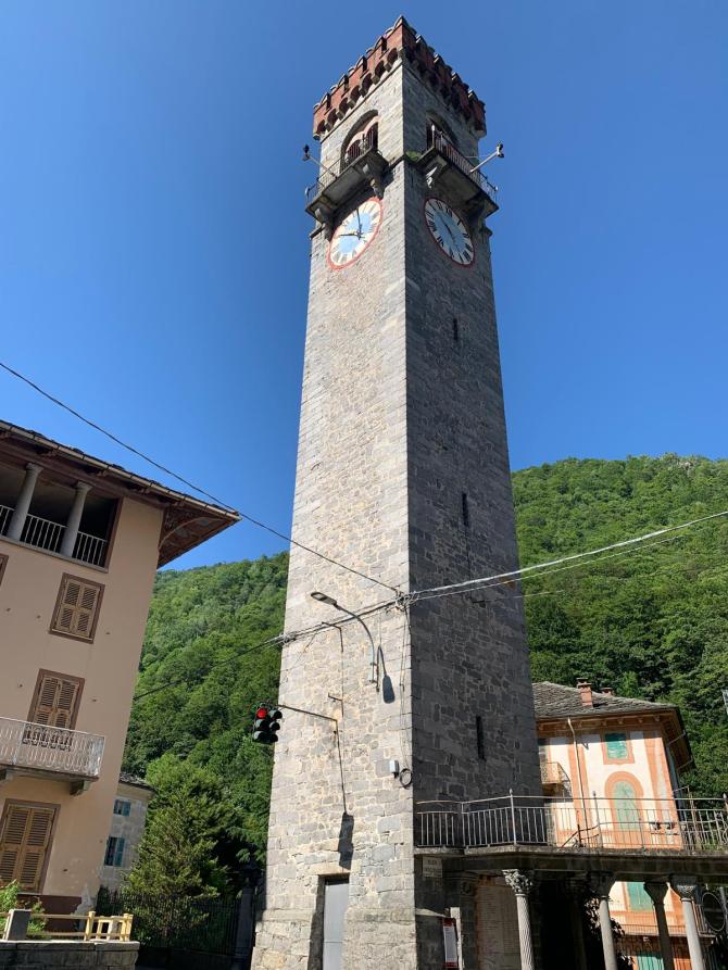 Rosazza (BI). La torre ghibellina del palazzo municipale in pietra grigia con merlature in mattoni rossi e orologio  con quadrante azzurro, bianco bordato di rosso 