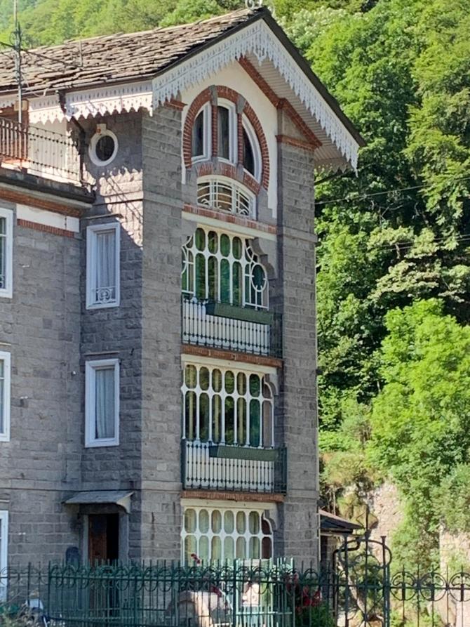 Rosazza (BI). Edificio a quattro piani con finestre bianche atipiche e decori in legno bianco che spiccano rispetto ai muri in pietra grigia 