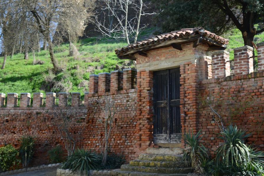 Sanfrè (CN). Parte della cinta muraria in mattoni con merlatura e porta d'ingresso rettangolare 