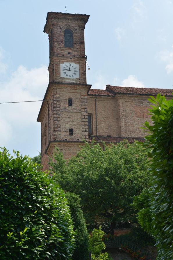 Sanfrè (CN). Dalle cime frondose degli alberi si intravede il campanile e parte della struttura in mattoni della parrocchia dei Santi Pietro e Paolo Apostoli 