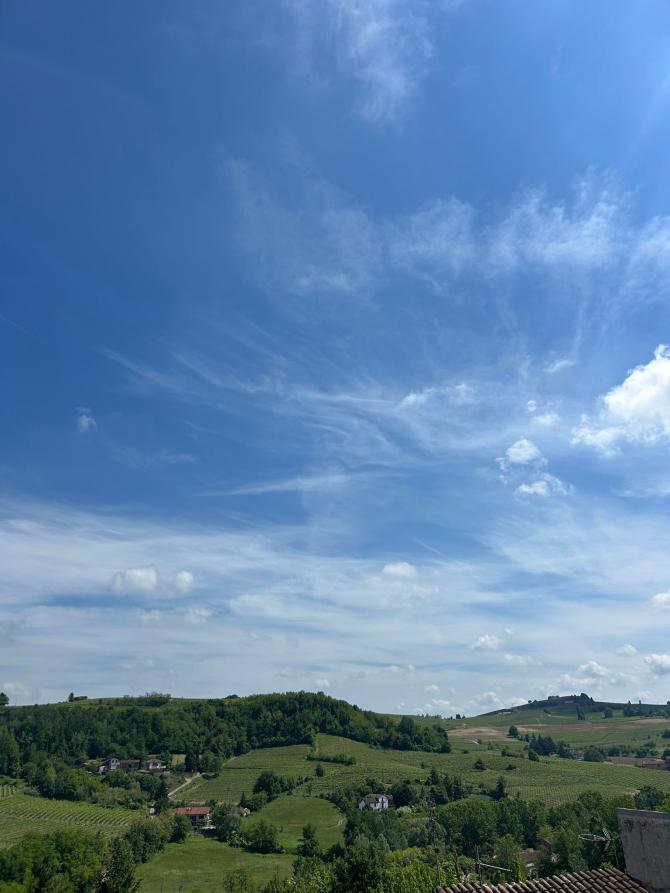 Castelletto Molina (ST). In primo piano in basso le colline verdeggianti e un cielo blu solcato da nuvole leggere 