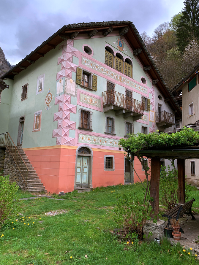 Mollia (VC). L'edificio storico Casa Belli decorato sui toni del rosa confetto. A destra una pergola con glicine 