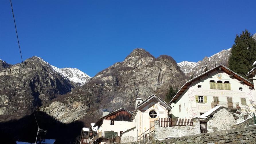 Mollia (VC). Scorcio panoramico invernale. Alcuni caseggati del paese sono illuminati dal sole. Sullo sfondo le montagne ormai brulle con le cime innevate. Il cielo è blu. Fotografia tratta dal sito del Comune (2026) 