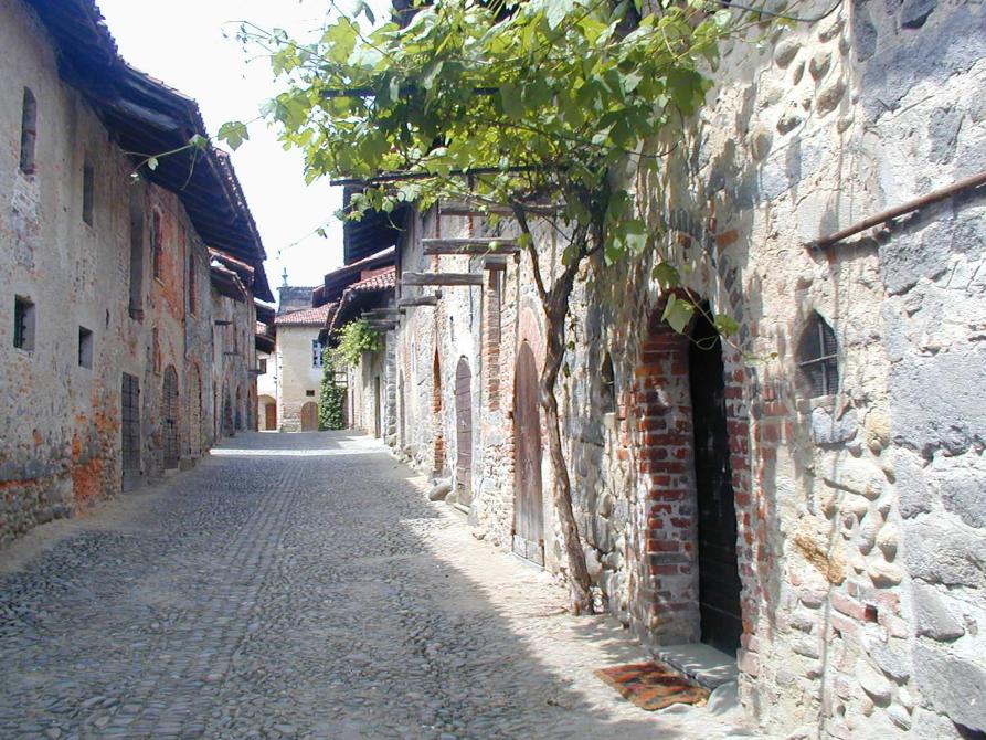 Candelo (BI). Ai lati della strada in ciottoli le case a due piani del Ricetto sono rivestite in pietra viva. A destra  una vite si arrampica sopra ad un portoncino d'entrata 