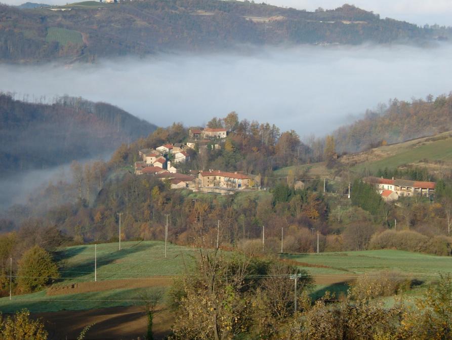 Mombarcaro (CN). Borgata Lunetta vista dall'alto e immersa nella natura rigogliosa. In lontananza la nebbia infilata fra le valli 