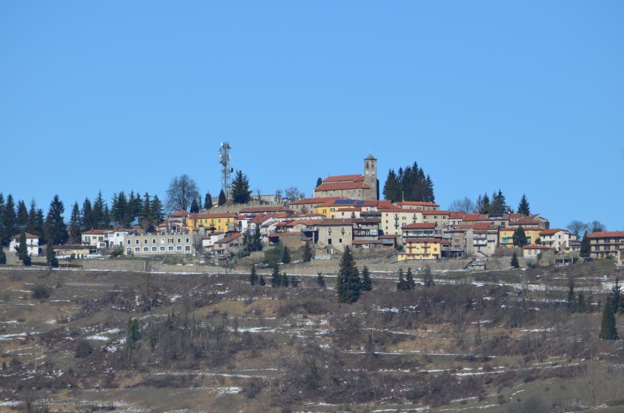 Mombarcaro (CN). Mombarcaro distesa sulla collina. I prati sono secchi e leggermente spruzzati dalla neve. Il cielo è azzurro intenso 