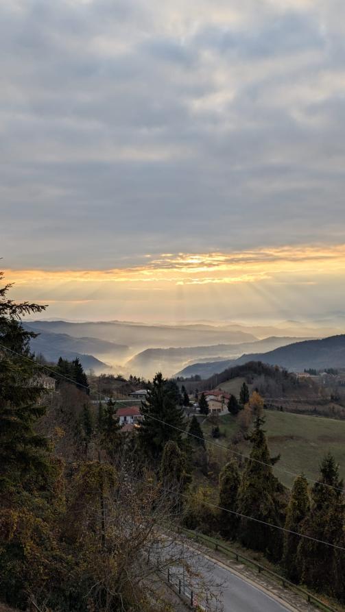 Mombarcaro (CN). I raggi del sole attraversano la coltre di nuvole tingendola di giallo. I profili delle colline, della case e degli alberi vengono evidenziati dalla luce.    