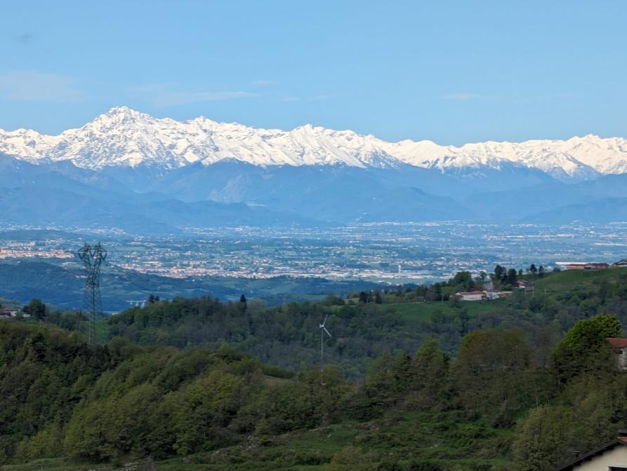Mombarcaro (CN). Vista panoramica delle montagne innevate che contrastano col cielo azzurro e la natura verdeggiante delle colline sottostanti 